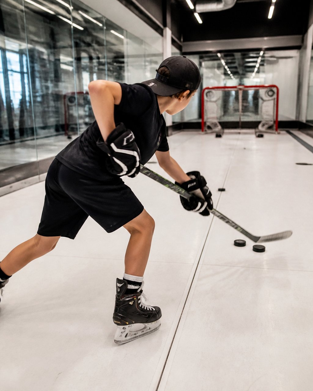 Young hockey player in shooting stance demonstrating proper weight transfer and upper-body rotation during shot execution in modern training facility